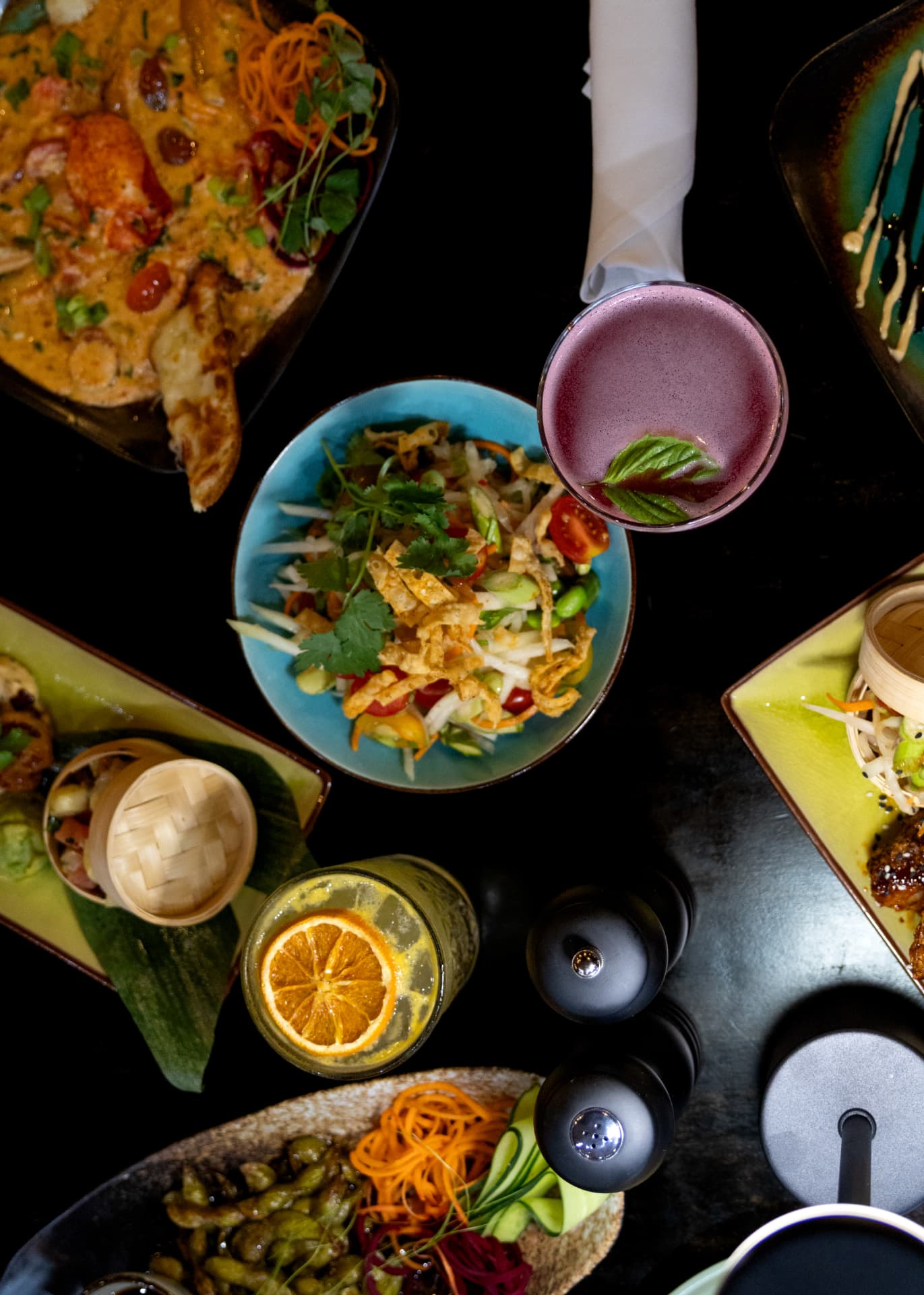 Papaya salad and a violet cocktail on a dark table