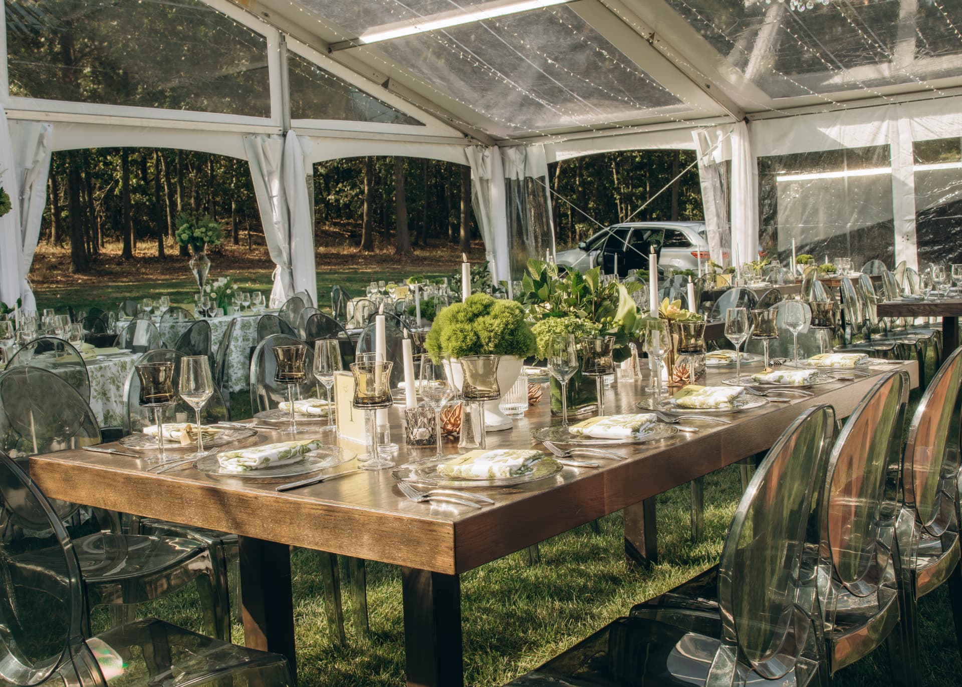 Harvest table set with candles and greenery under a clear event tent