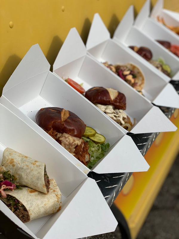 Food truck boxes with pretzel-bun sandwiches, tacos and a steak wrap