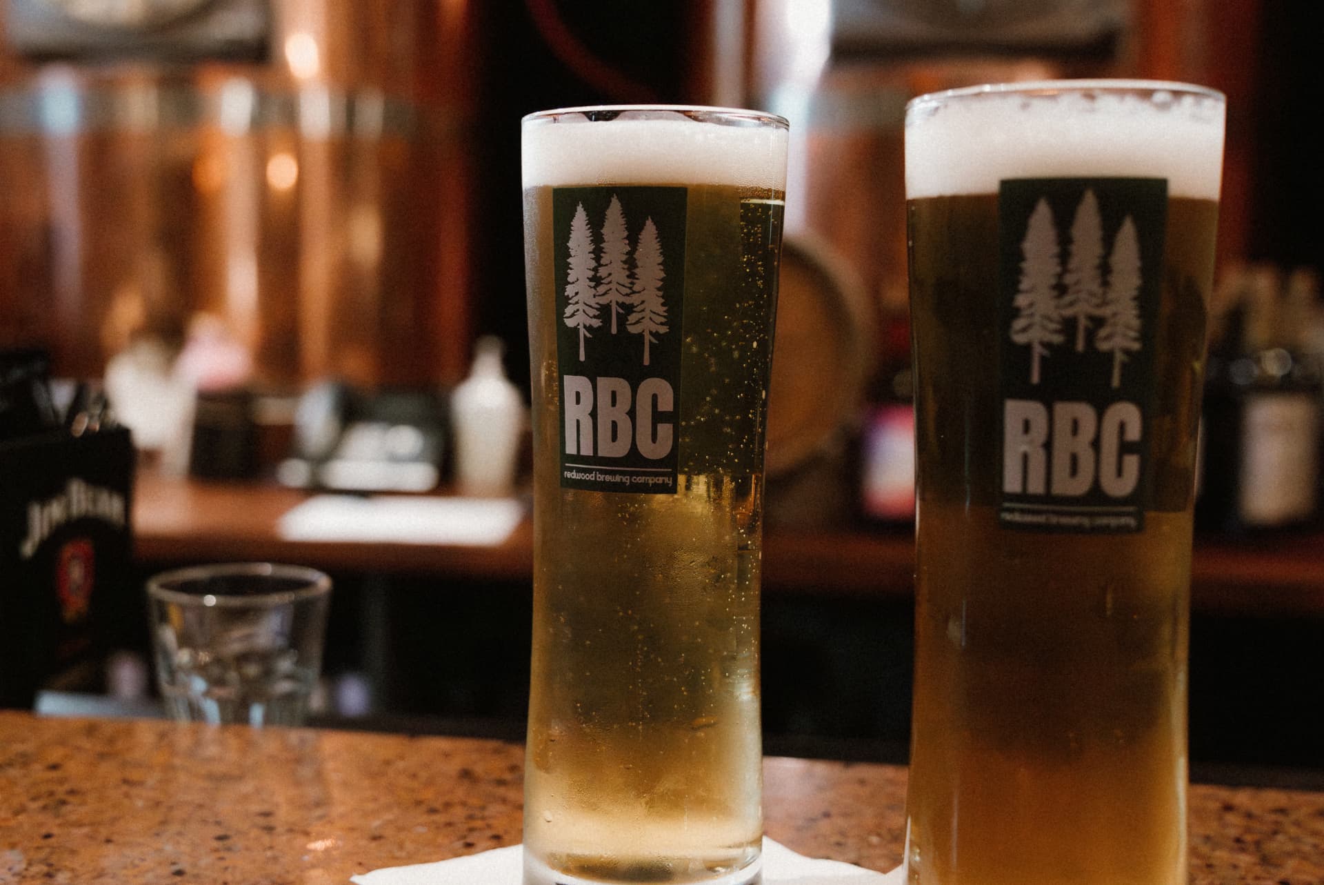 Two RBC pilsner glasses on the bar in front of the copper brewhouse