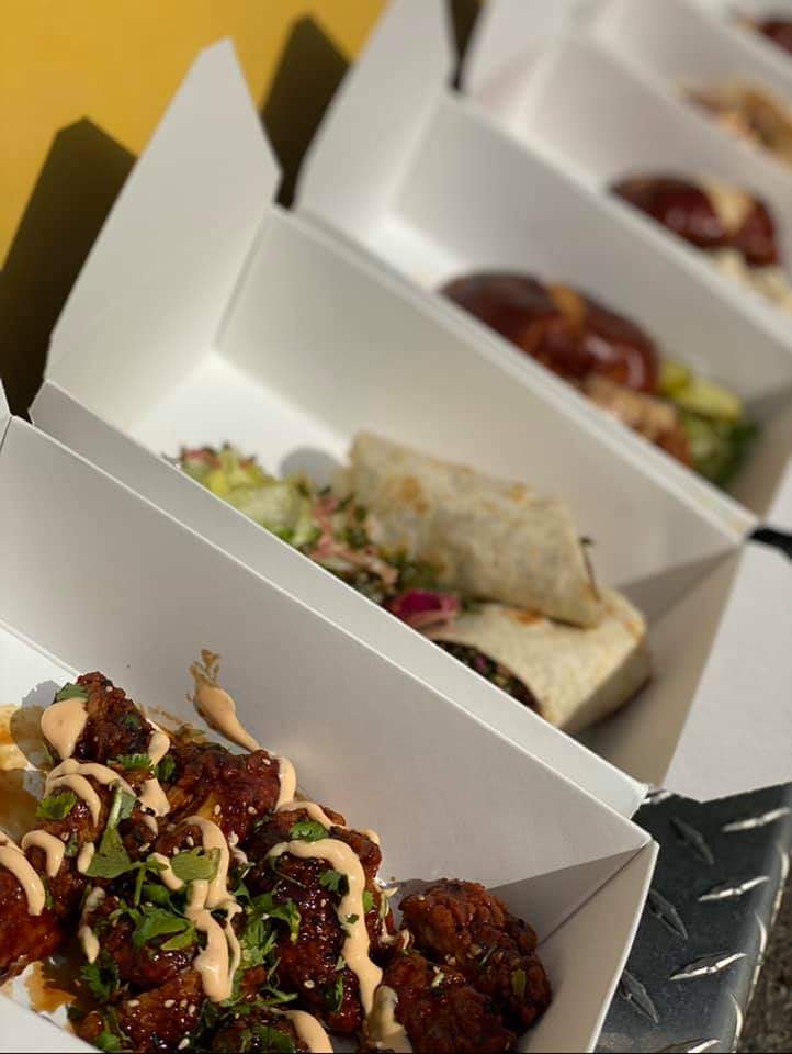 Food truck boxes with sesame chili wings, a wrap and pretzel-bun sandwiches
