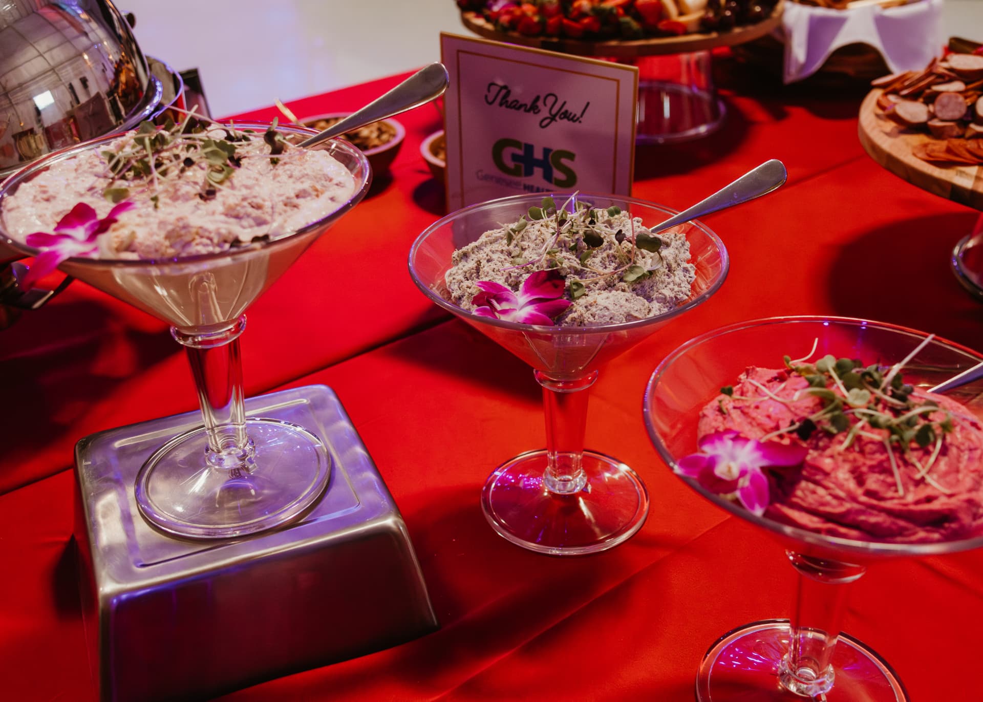 Martini-glass dips garnished with orchids and microgreens on a red buffet