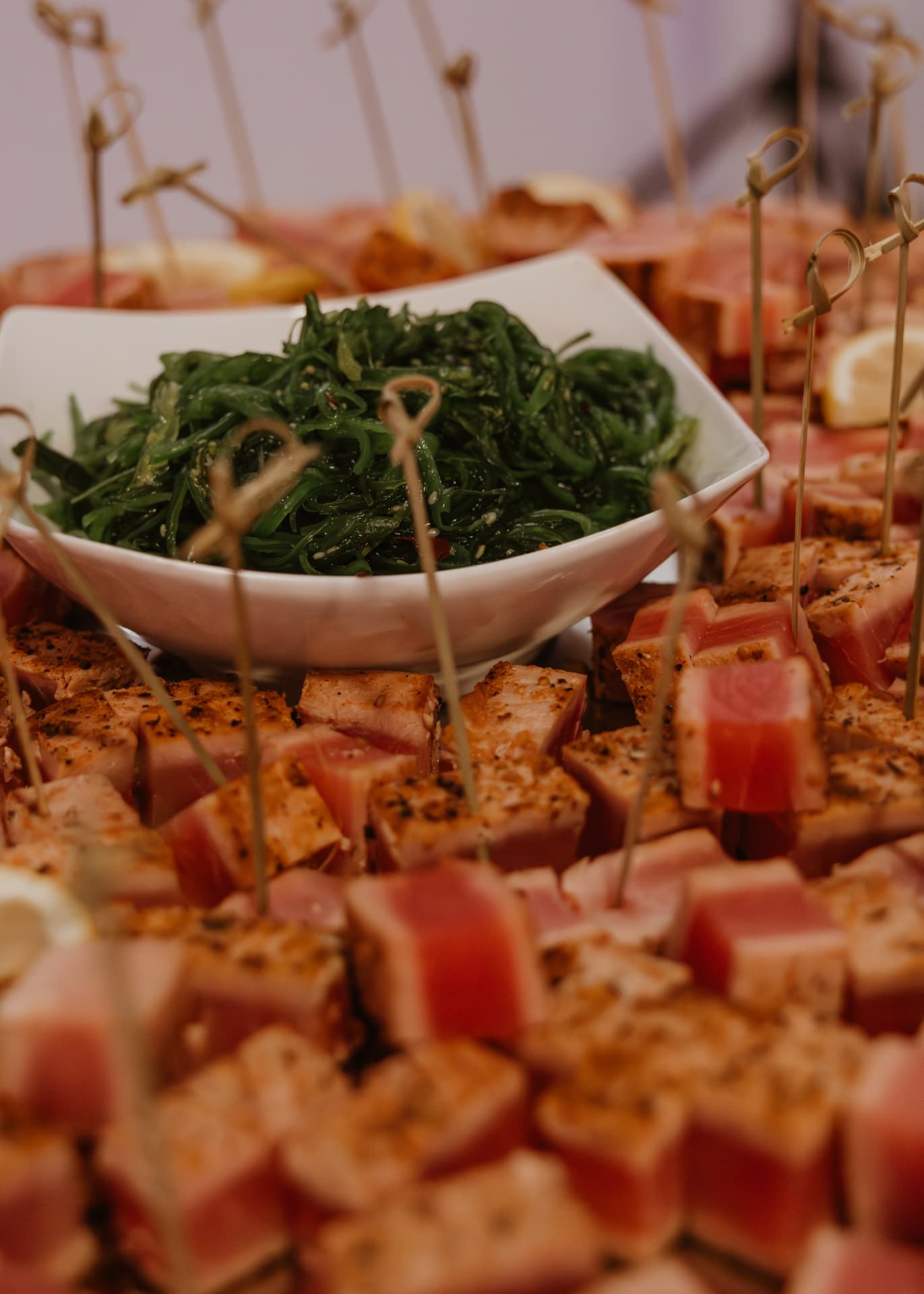 Skewered seared tuna bites around a bowl of seaweed salad
